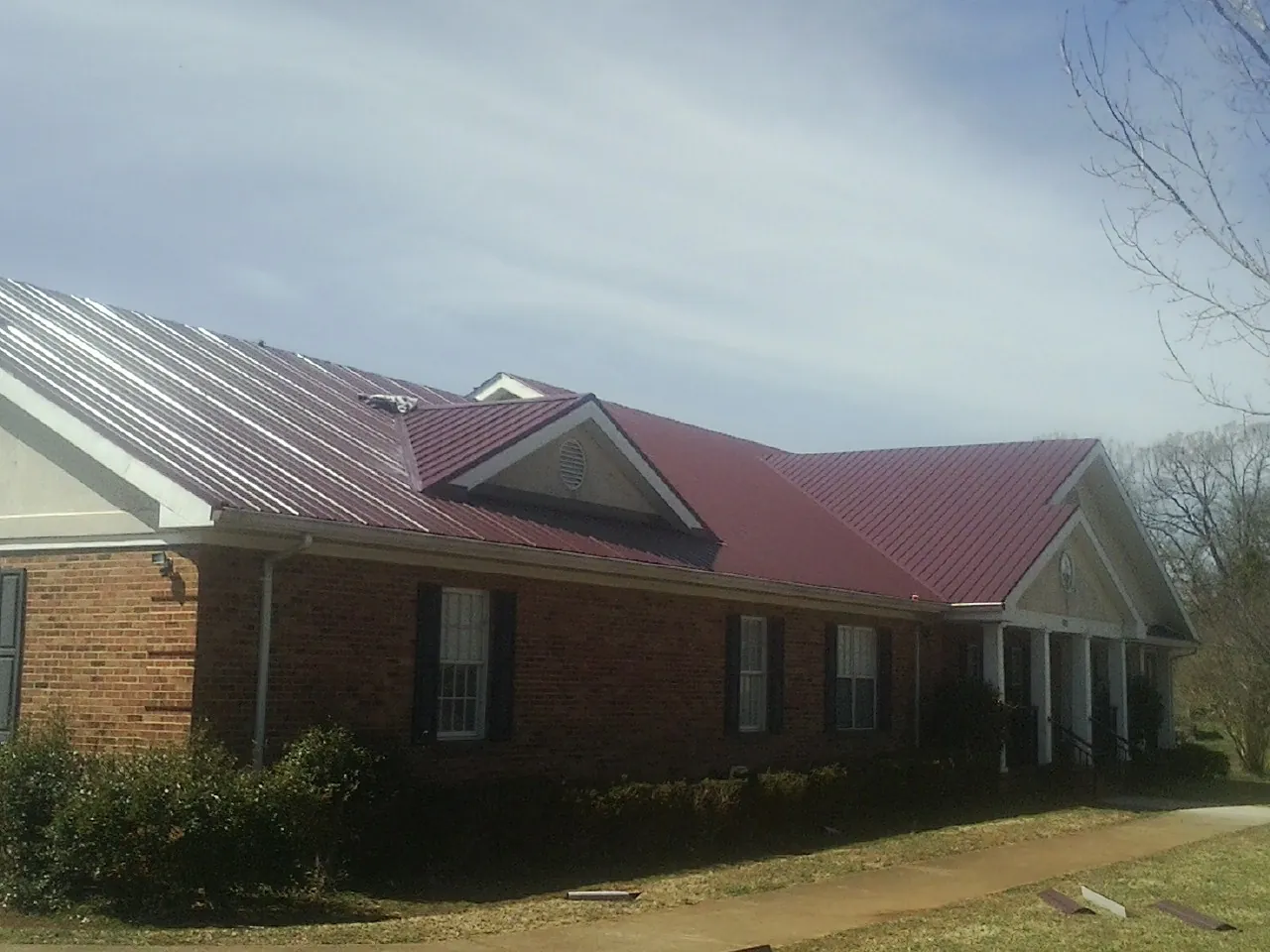 Red metal roof with gabled entries on a long brick building, from a Hail Damage Roof Repair job in Pleasant Valley
