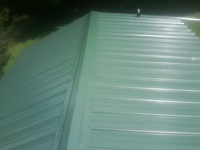 New green metal panels meeting at the ridge of a roof — Flat Roof Repair work by our crew in Pleasant Valley
